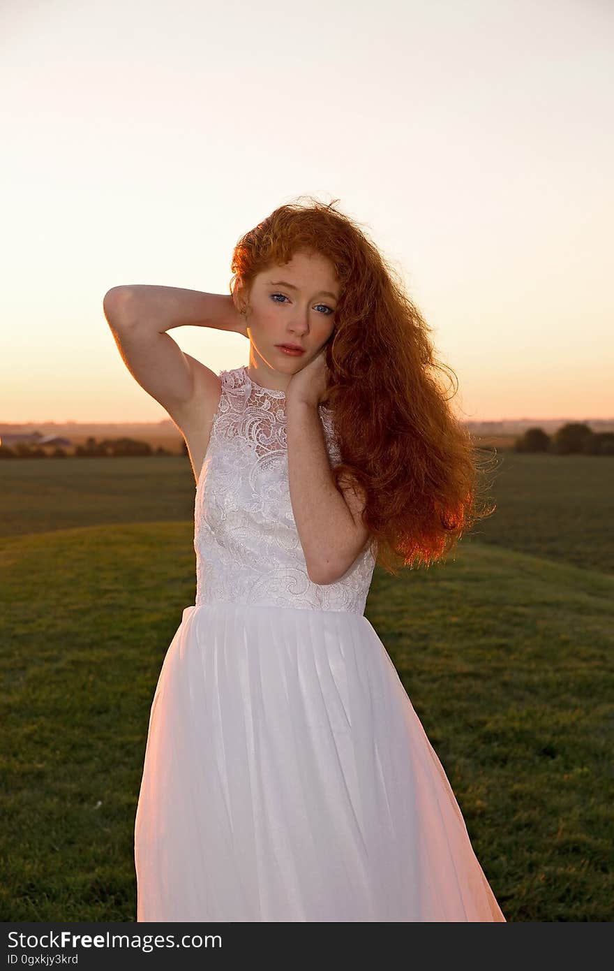 A woman standing on a field wearing a white dress at sunset. A woman standing on a field wearing a white dress at sunset.