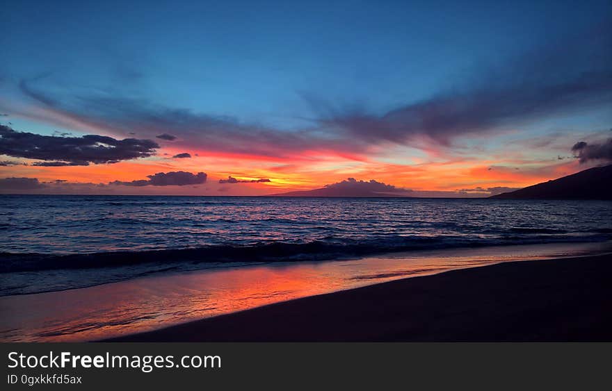 Sunset over beach waterfront with blue skies.