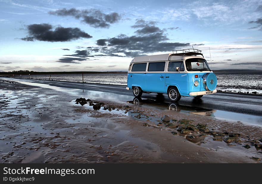 A blue retro campervan driving along a muddy beach at dusk. A blue retro campervan driving along a muddy beach at dusk.