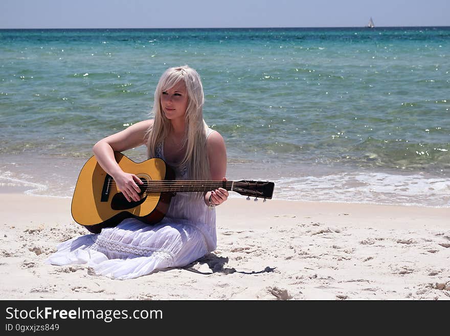 Blond Woman Playing Spruce Top Dreadnought Acoustic Guitar by the Seashore