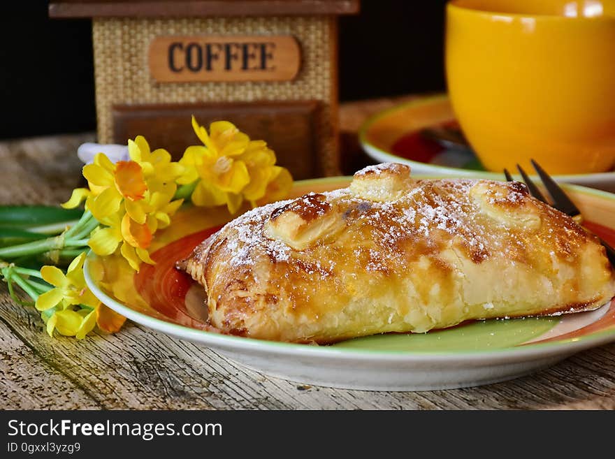 Baked puff pastry and fork on plate with daffodils next to yellow coffee cup. Baked puff pastry and fork on plate with daffodils next to yellow coffee cup.