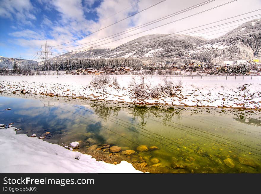 Utility stanchions through snow covered mountain landscape reflecting in small stream on sunny day. Utility stanchions through snow covered mountain landscape reflecting in small stream on sunny day.