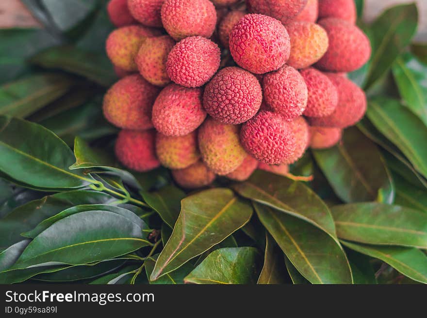 Fresh organic lychee fruit and lychee leaves on a rustic wooden background.