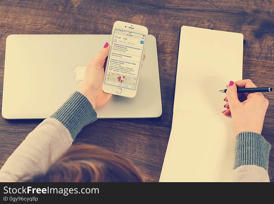 Overhead of woman holding cellphone in one hand and pen over blank notebook on in other on wooden desktop with computer. Overhead of woman holding cellphone in one hand and pen over blank notebook on in other on wooden desktop with computer.