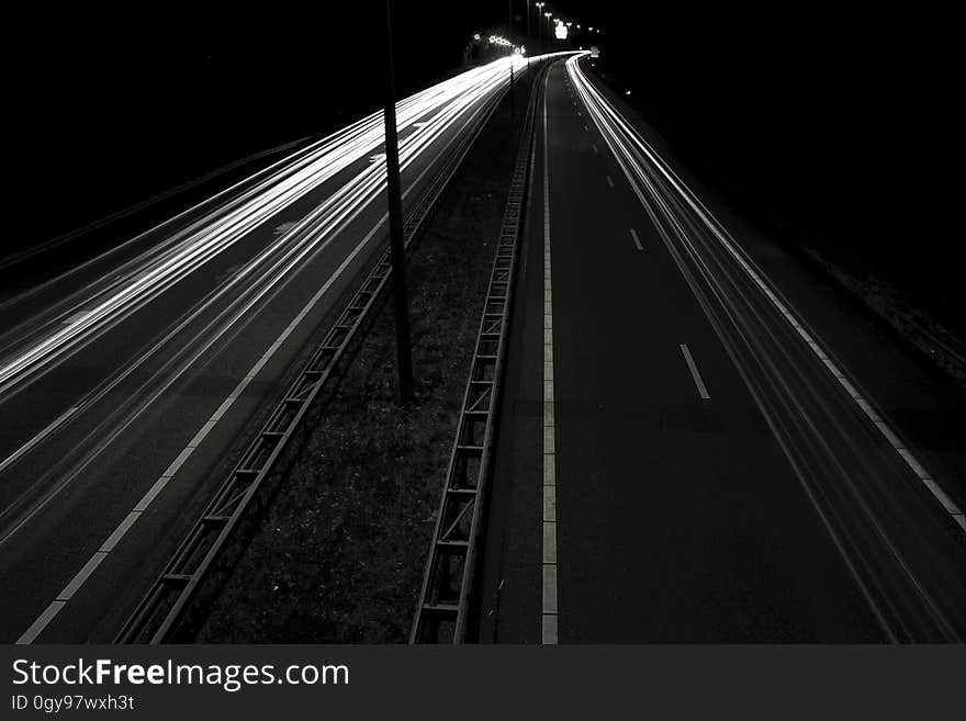 White streaks from blur of headlights on dark roadway at night in black and white. White streaks from blur of headlights on dark roadway at night in black and white.