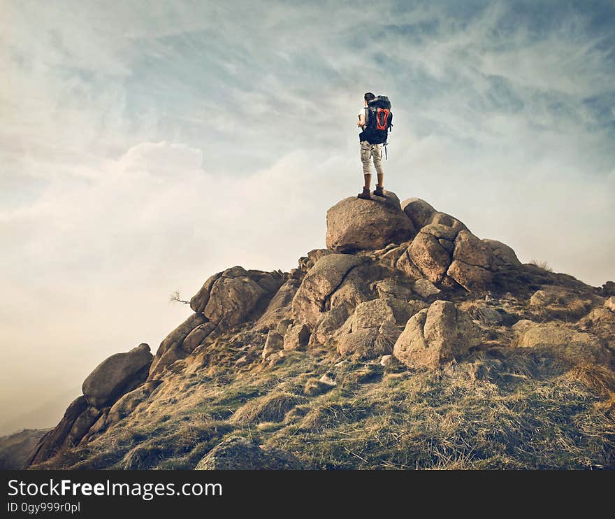 Solitary climber with large rucksack and well equipped, on a rock on the mountain peak (maybe taking a photograph), thin cloud and touch of blue sky. Solitary climber with large rucksack and well equipped, on a rock on the mountain peak (maybe taking a photograph), thin cloud and touch of blue sky.