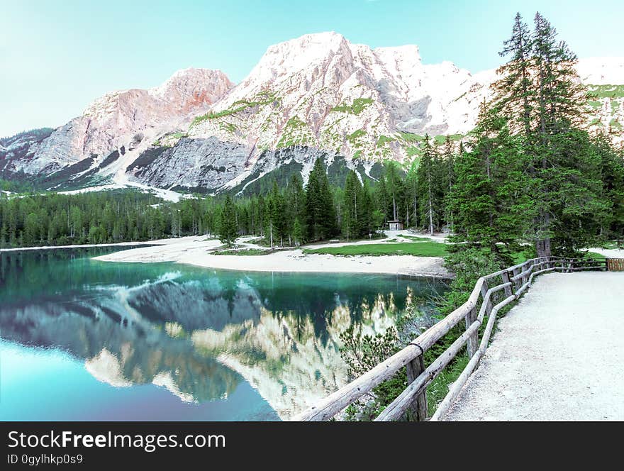 Mountains reflecting in calm waters of alpine lake with bridge and pine trees along banks. Mountains reflecting in calm waters of alpine lake with bridge and pine trees along banks.