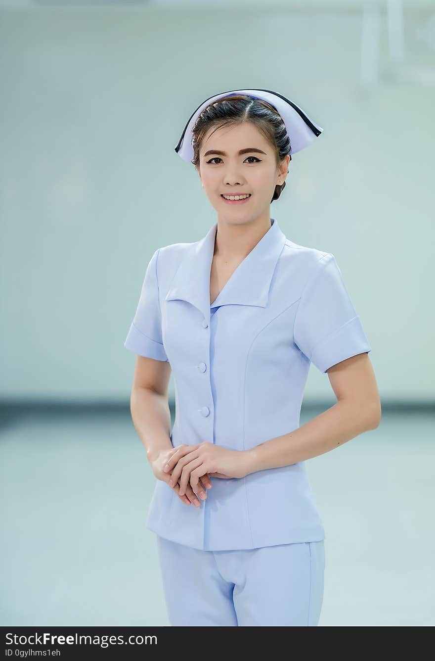 Indoor portrait of female nurse standing in uniform and hat with smile.