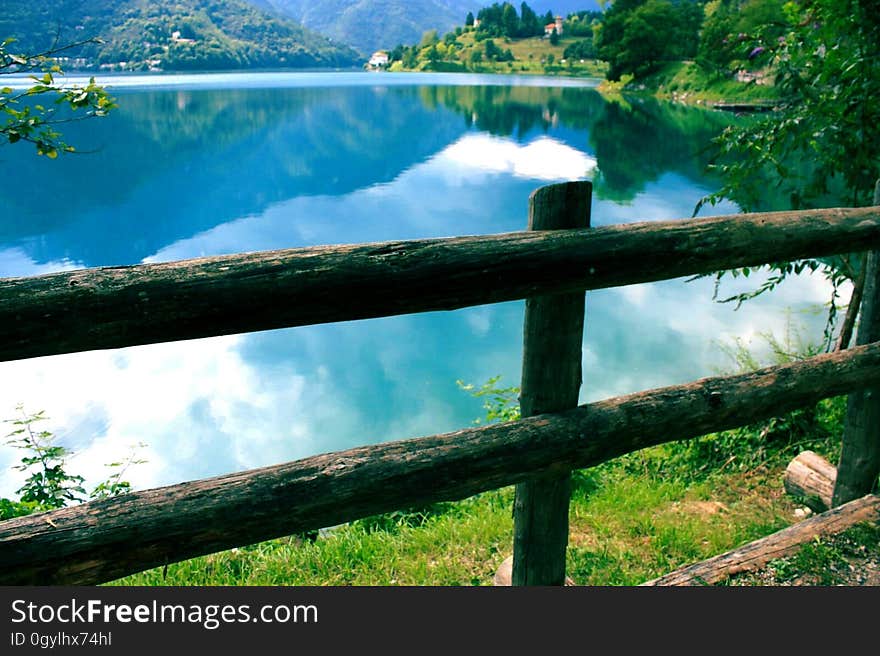 A wooden fence on the lake coast and hills and clouds reflecting on the water surface in the background. A wooden fence on the lake coast and hills and clouds reflecting on the water surface in the background.