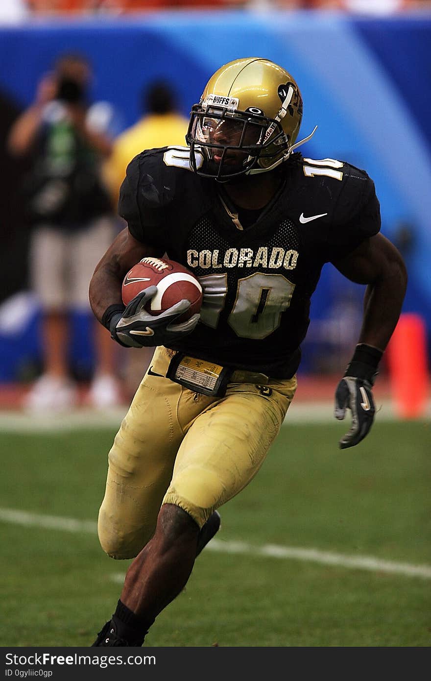 Closeup of a college player on the Colorado team running at an angle during a game with the football cradled in his right arm. Closeup of a college player on the Colorado team running at an angle during a game with the football cradled in his right arm.