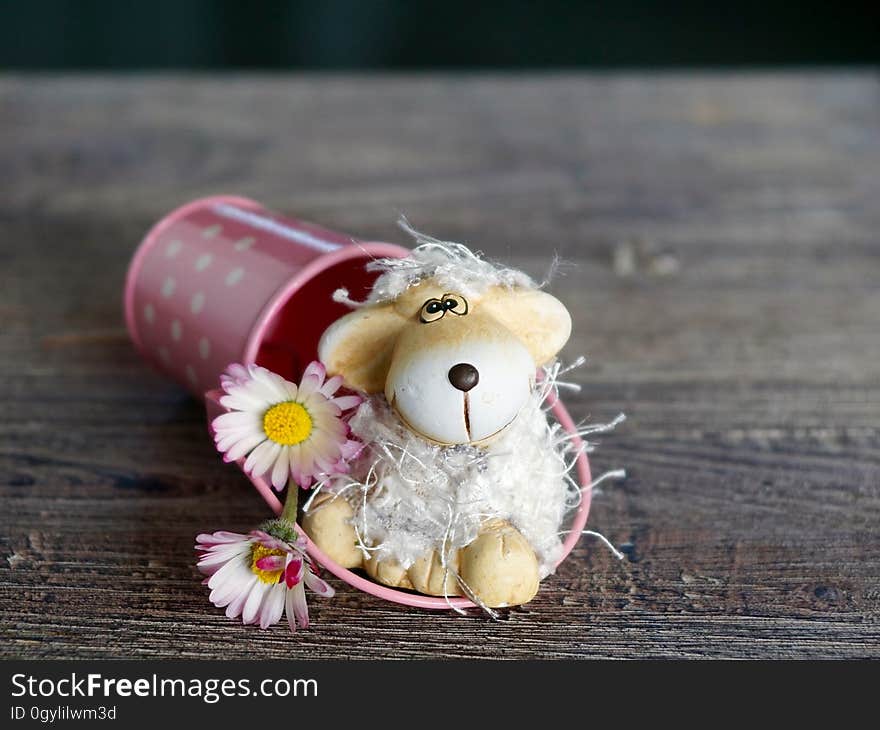 Closeup of cute puppy dog (stuffed) toy emerging from a purple bucket decorated with daisy flowers, all on a brown grainy wooden table. Closeup of cute puppy dog (stuffed) toy emerging from a purple bucket decorated with daisy flowers, all on a brown grainy wooden table.