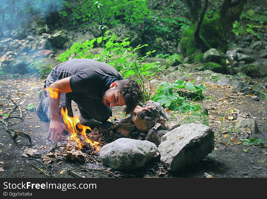 Camping man making fire in countryside, breathing on flames.