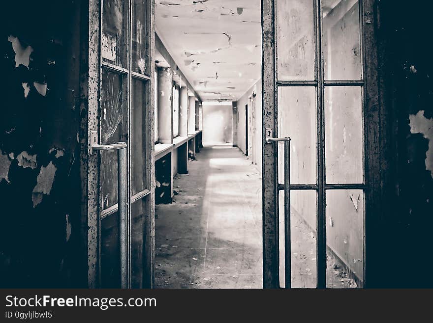 Open glass door leading into a corridor of a derelict building with paint peeling off the walls and ceiling everywhere. Open glass door leading into a corridor of a derelict building with paint peeling off the walls and ceiling everywhere.