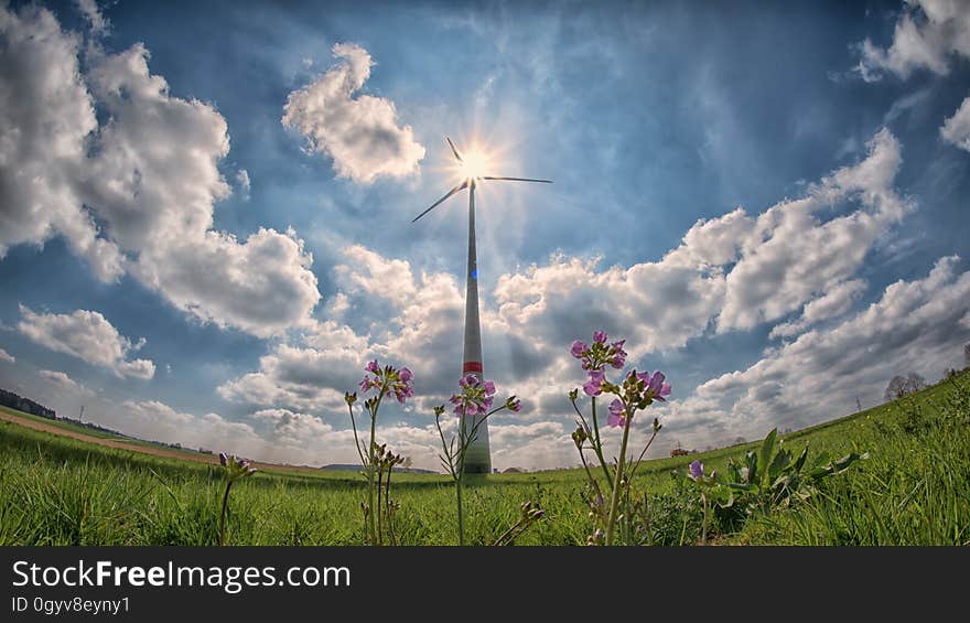 Fish eye view of wind turbine in countryside field with sun shining through blades and cloudscape background.