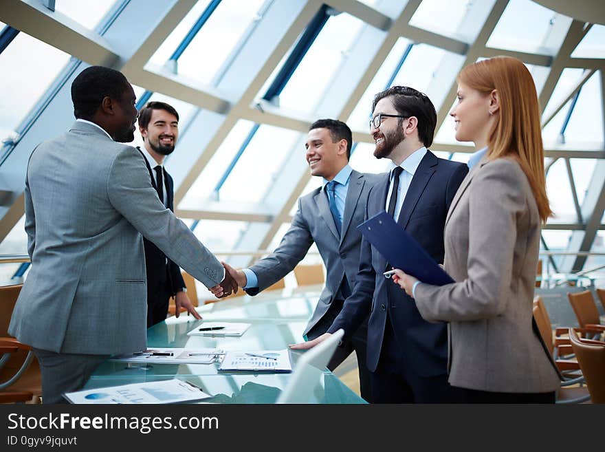 Business professionals shaking hands standing around conference room table.