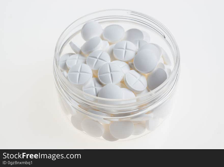 A transparent cup with white pills. A transparent cup with white pills.