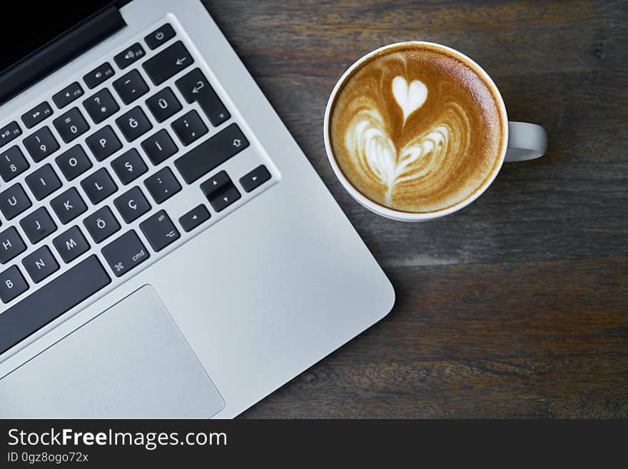 Coffee mug with heart shape in foam next to open laptop computer. Coffee mug with heart shape in foam next to open laptop computer.