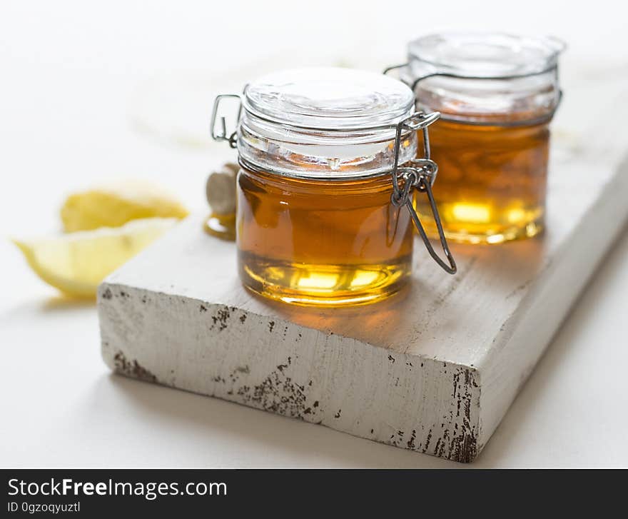 Close up of jars of honey on rustic wooden board with lemon wedges.
