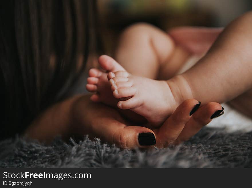 Close up of woman's hands holding feet of newborn baby on carpet. Close up of woman's hands holding feet of newborn baby on carpet.