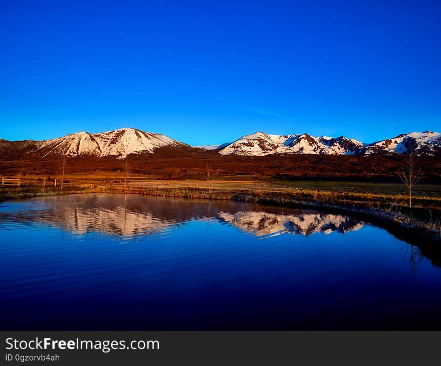 A view of mountains reflecting on a still lake surface. A view of mountains reflecting on a still lake surface.