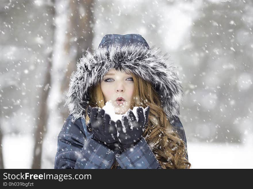 Portrait of pretty blond woman in warm jacket with fur hood posing in a snow storm. Portrait of pretty blond woman in warm jacket with fur hood posing in a snow storm.