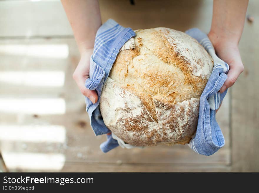 Hands with two blue cloths holding a loaf of hot bread straight out of the oven. Hands with two blue cloths holding a loaf of hot bread straight out of the oven.