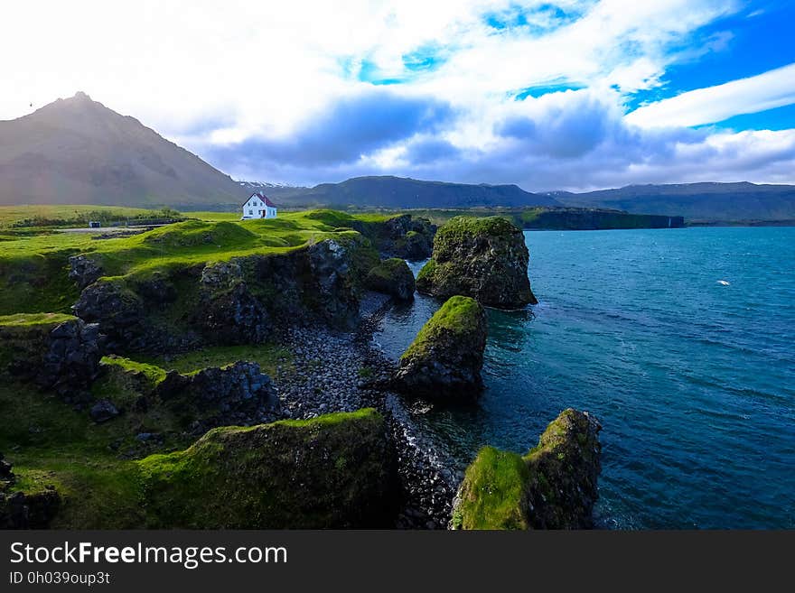 Aerial of white house on edge of cliff overlooking waterfront against blue skies. Aerial of white house on edge of cliff overlooking waterfront against blue skies.