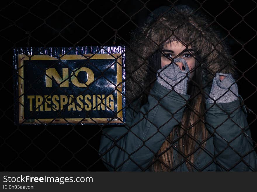 Young woman looking through fence at night next to no trespassing sign. Young woman looking through fence at night next to no trespassing sign.