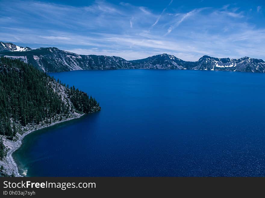 Aerial view of blue crater lake with pine tree forest in snow against blue skies on sunny day.
