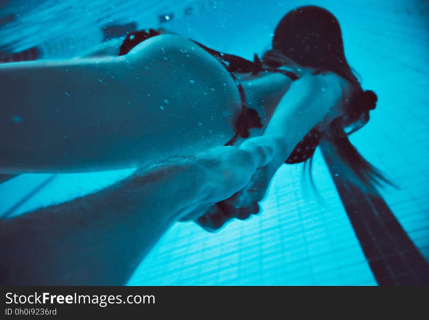 Woman swimming underwater holding hands with someone.