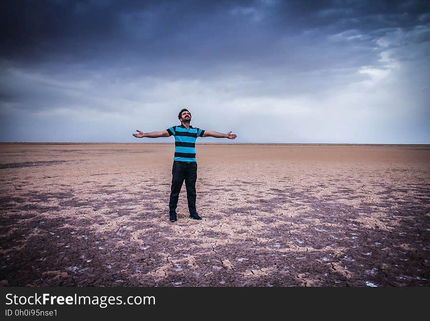 Man in black and blue striped shirt and pants standing in desert with open arms against clouds in blue sky. Man in black and blue striped shirt and pants standing in desert with open arms against clouds in blue sky.