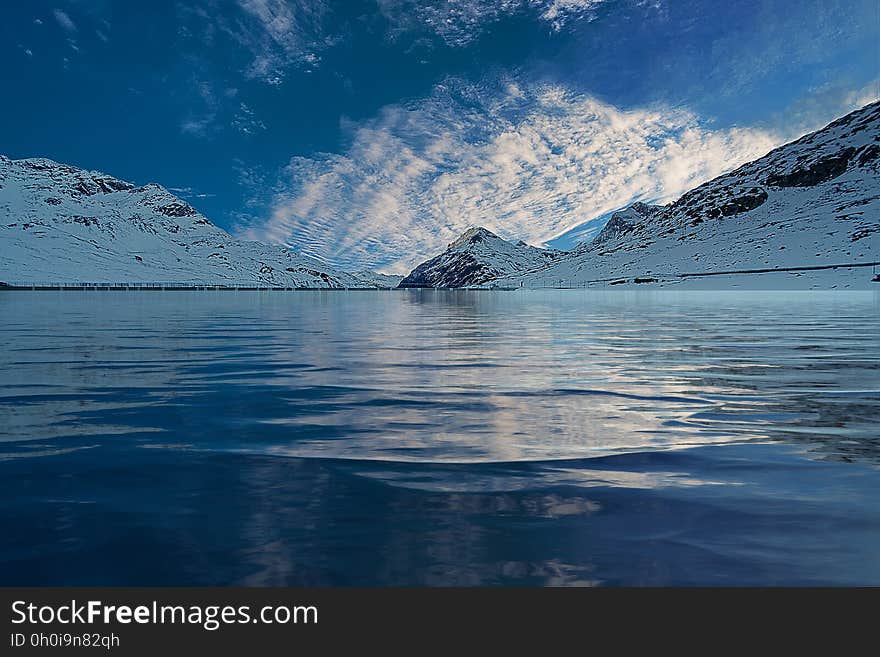 Clouds reflecting in blue waters of alpine lake with snow covered peaks on sunny day. Clouds reflecting in blue waters of alpine lake with snow covered peaks on sunny day.