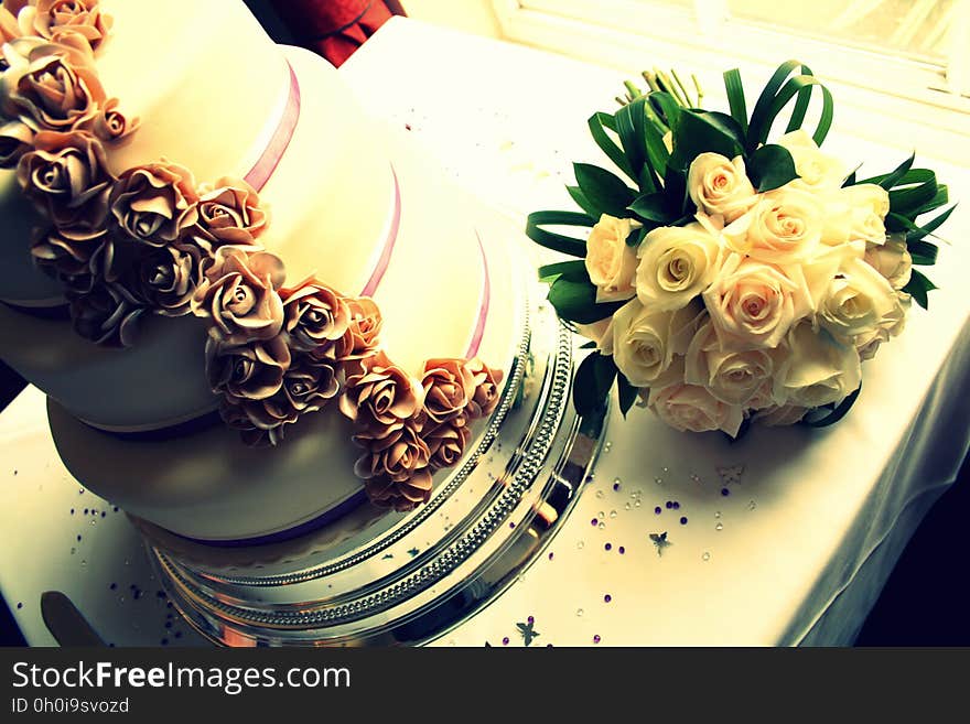 Bridal bouquet of white roses next to tiered wedding cake on table. Bridal bouquet of white roses next to tiered wedding cake on table.