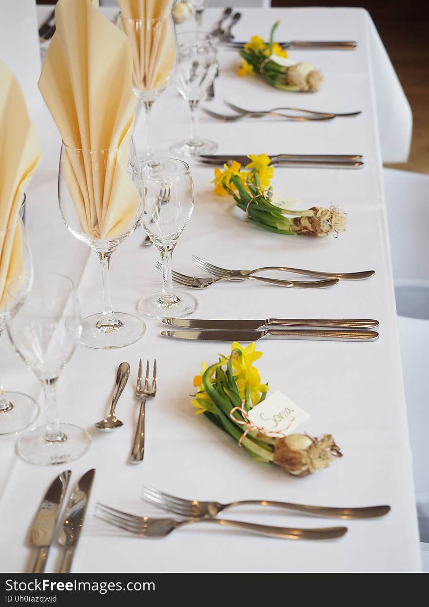 Table set for formal dinner with linens, silverware and glasses with bouquet of daffodils and name tags. Table set for formal dinner with linens, silverware and glasses with bouquet of daffodils and name tags.