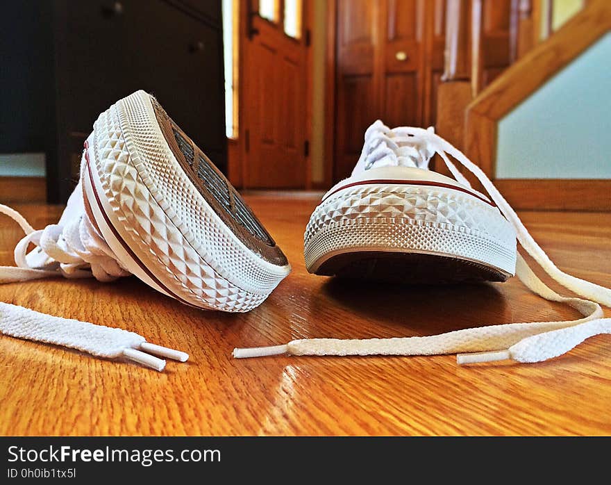 Close up of Converse white sneakers on wooden floor inside house.