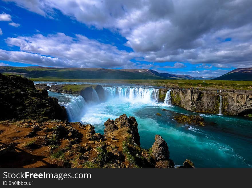 Scenic view of cascading waterfall down steep cliffs on wide river with cloudscape background. Scenic view of cascading waterfall down steep cliffs on wide river with cloudscape background.