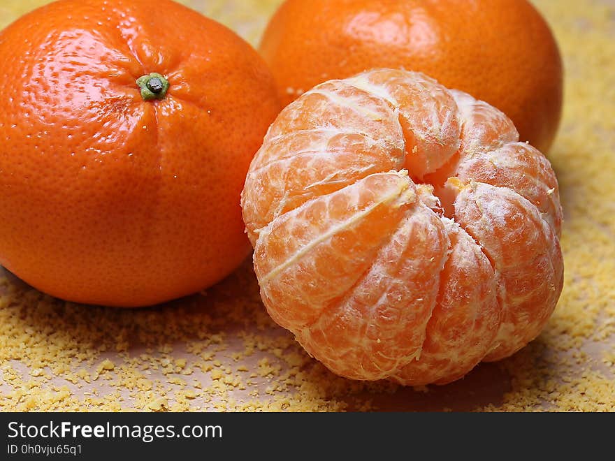 A peeled mandarin next to a couple of unpeeled ones.