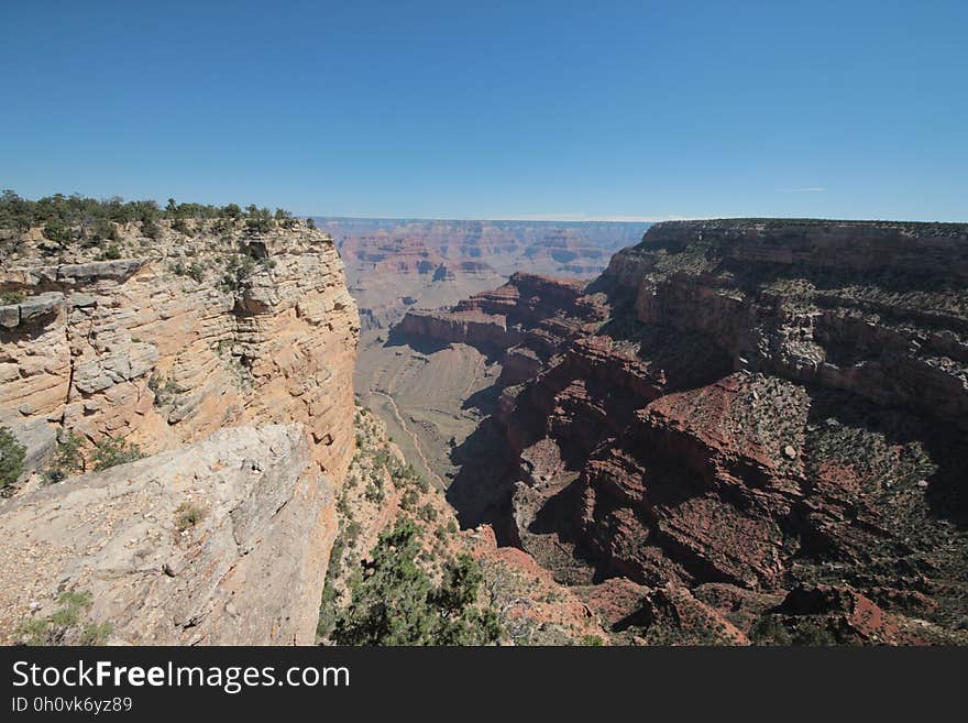 Rocky, sandy desert landscape with steep unstable cliff on the left and massive dark rock on right with a narrow valley with scrub lying in between, cloudless blue sky. Rocky, sandy desert landscape with steep unstable cliff on the left and massive dark rock on right with a narrow valley with scrub lying in between, cloudless blue sky.