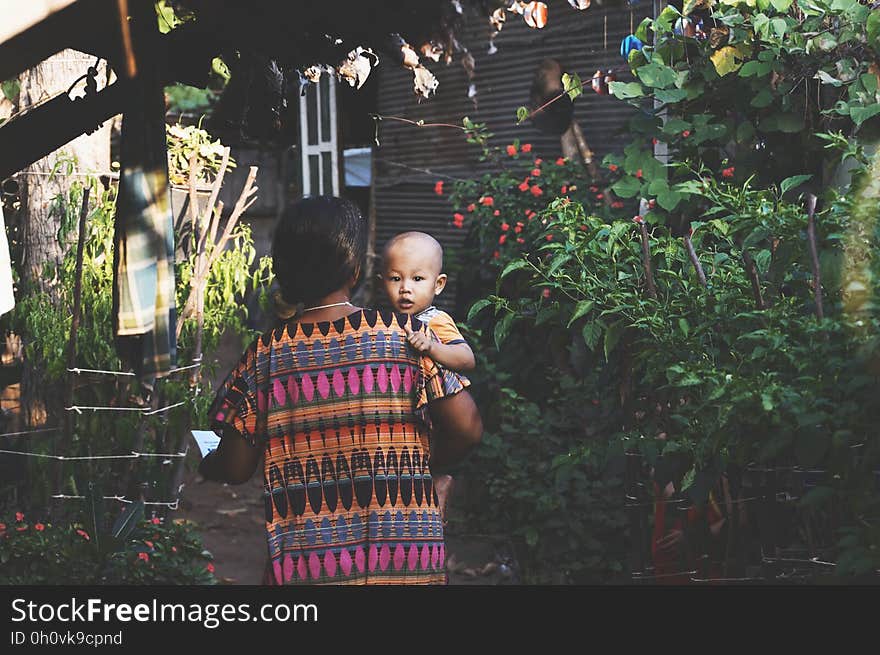 Woman in Orange Pink Aztec Dress Carrying Child in Orange Shirt