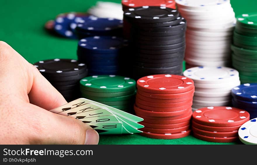 A person looking at their hand during a poker game with lot of playing chips on the table. A person looking at their hand during a poker game with lot of playing chips on the table.