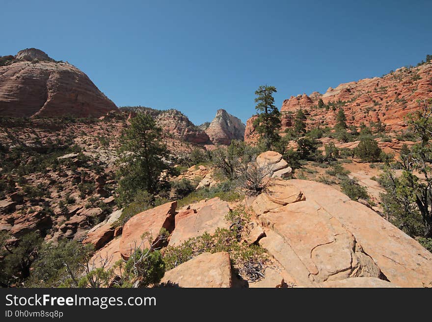 Red sandstone, rocks, sand and scrub making a barren desert landscape with red cliffs, blue cloudless sky. Red sandstone, rocks, sand and scrub making a barren desert landscape with red cliffs, blue cloudless sky.