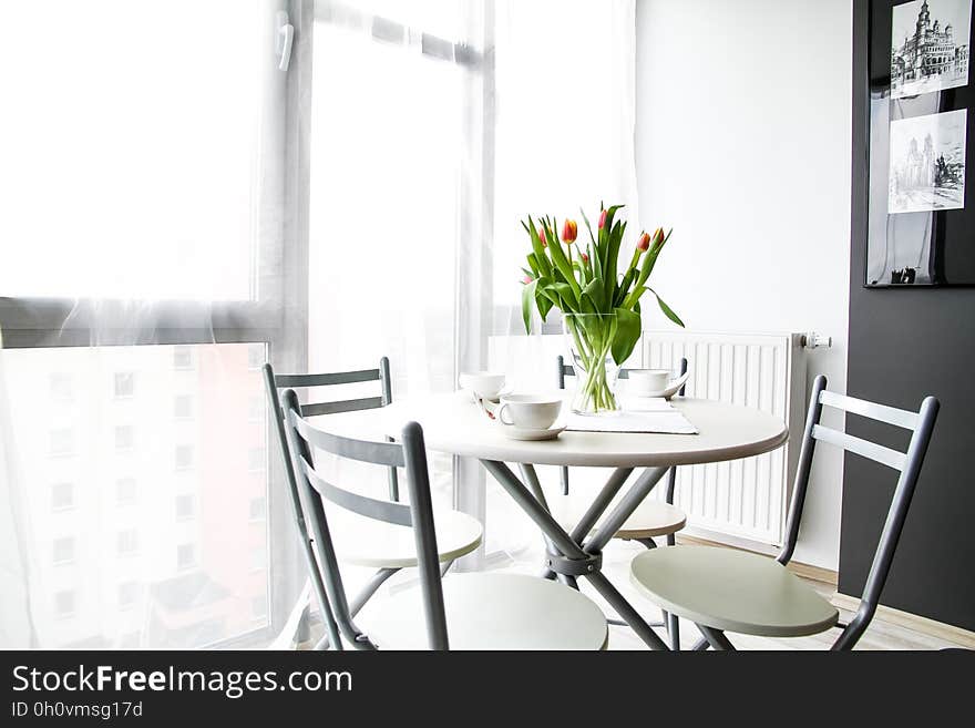 Table and chairs with white china cups and cut flowers in vase inside sunny room. Table and chairs with white china cups and cut flowers in vase inside sunny room.