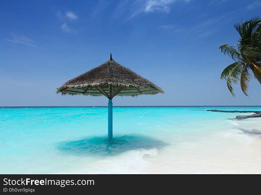 A straw parasol in the water on a tropical beach. A straw parasol in the water on a tropical beach.