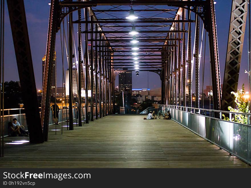 Couple sitting on illuminated bridge in city at night.