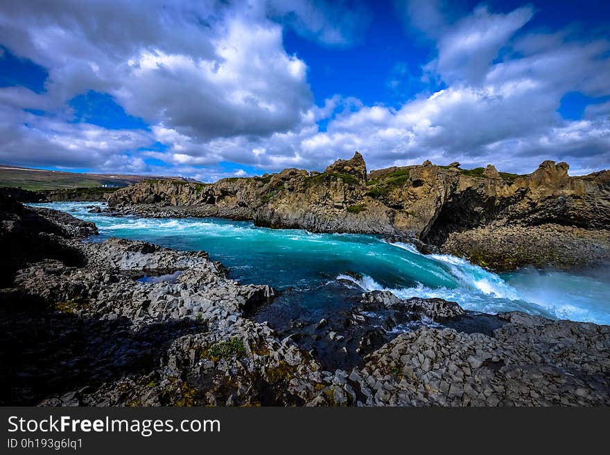 River with rocky shores in countryside against blue skies on sunny day.