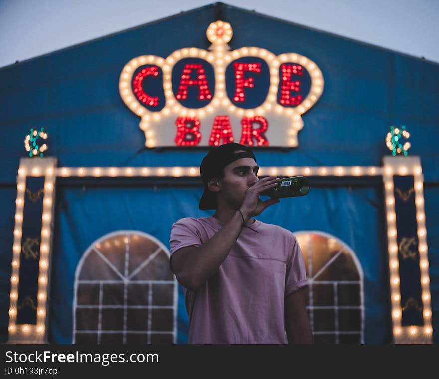 Young man drinking from bottle standing outside cafe or bar. Young man drinking from bottle standing outside cafe or bar.