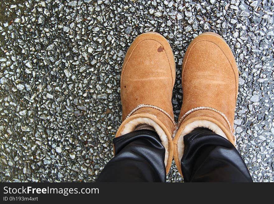 Feet in brown fleece lined boots standing on pavement from above. Feet in brown fleece lined boots standing on pavement from above.