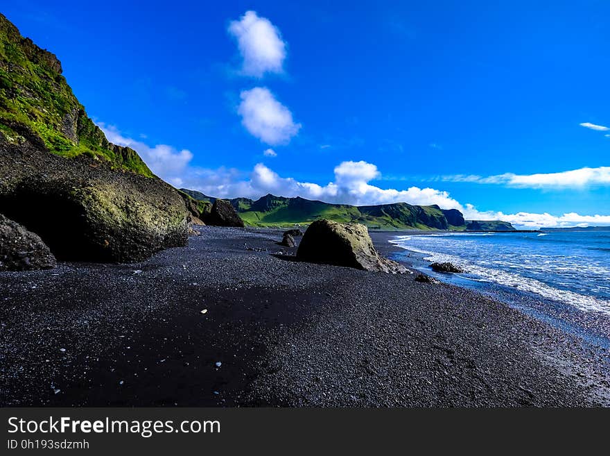 Waves on rocky beach against steep green cliffs on sunny day with blue skies. Waves on rocky beach against steep green cliffs on sunny day with blue skies.