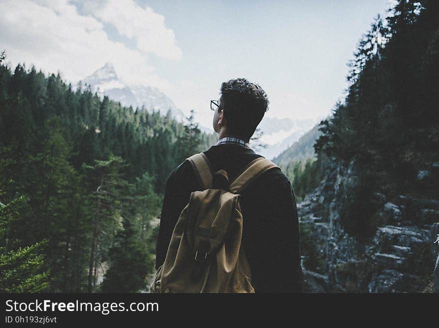 Back view of an anonymous adult male wearing a backpack, standing at a valley vista viewing the mountain landscapes that surround him. Back view of an anonymous adult male wearing a backpack, standing at a valley vista viewing the mountain landscapes that surround him.