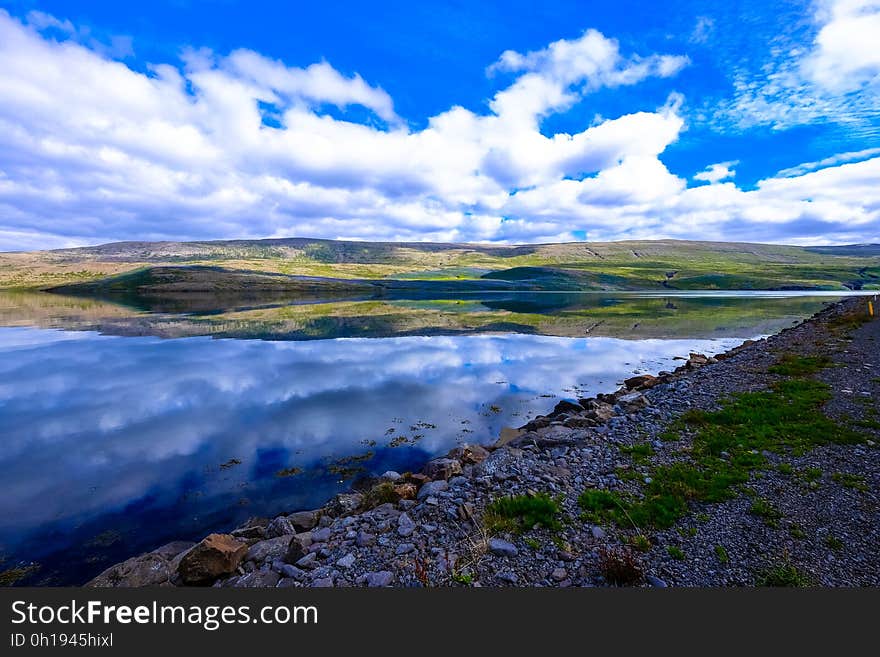 Clouds in blue skies reflecting in lake in green country fields on sunny day. Clouds in blue skies reflecting in lake in green country fields on sunny day.